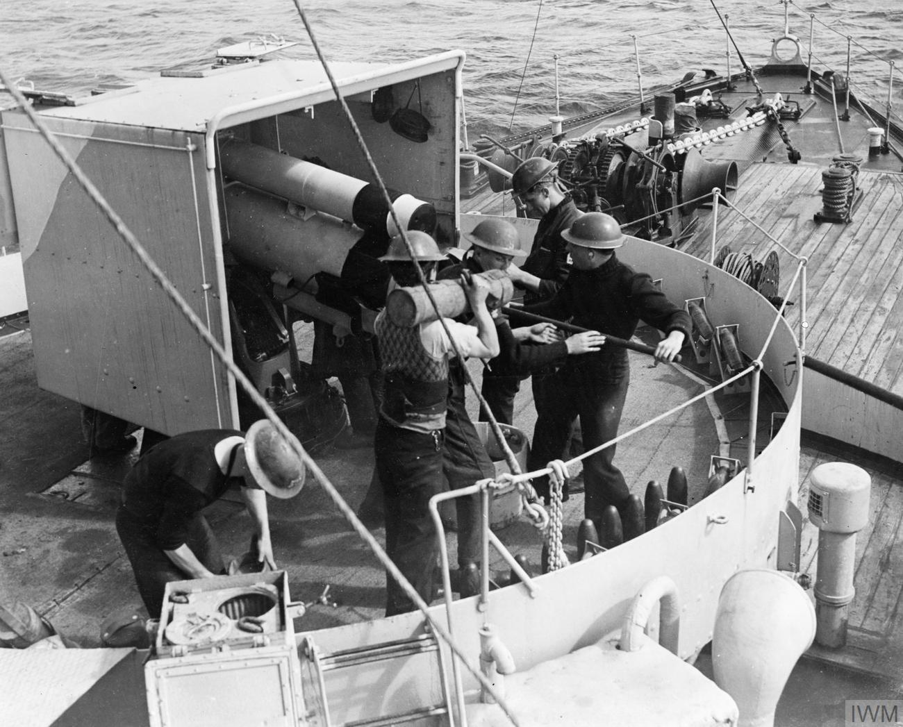 Six sailors in steel helmets loading a 4-inch gun on the forecastle of a corvette at sea